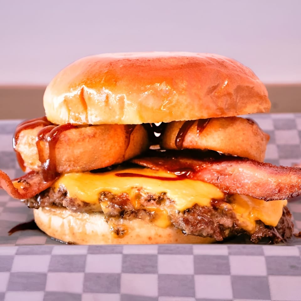 Made Burgers' bacon cheeseburger with onion rings and barbecue sauce on a checkered wrapper.