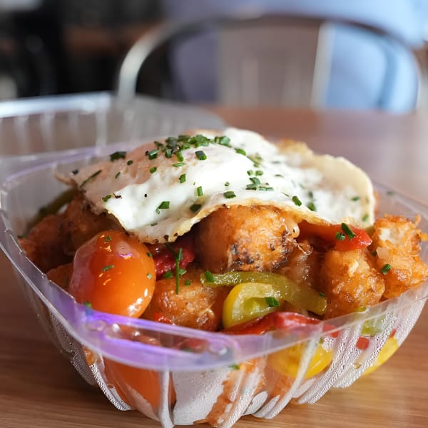 Made Burgers' tater tots with bell peppers, cherry tomatoes, and a fried egg in a plastic container.