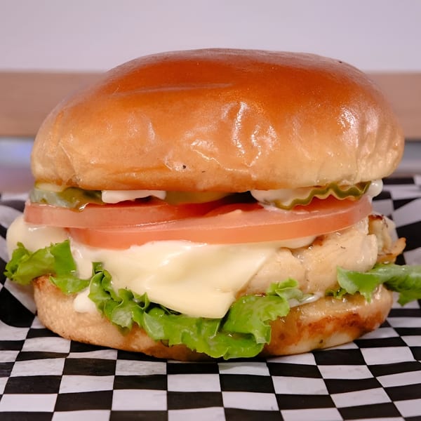 A Made Burgers chicken sandwich with melted cheese, lettuce, tomato, and pickles on a checkered wrapper.