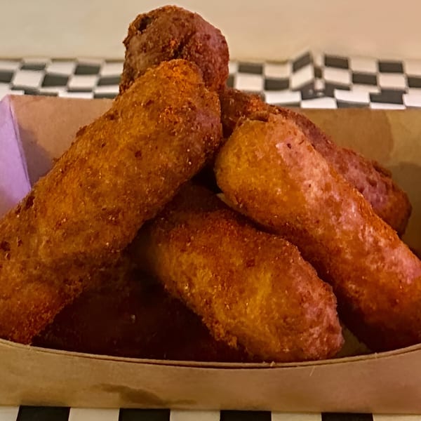 Golden brown Made Burgers corn dogs piled in a paper tray on a checkered surface.