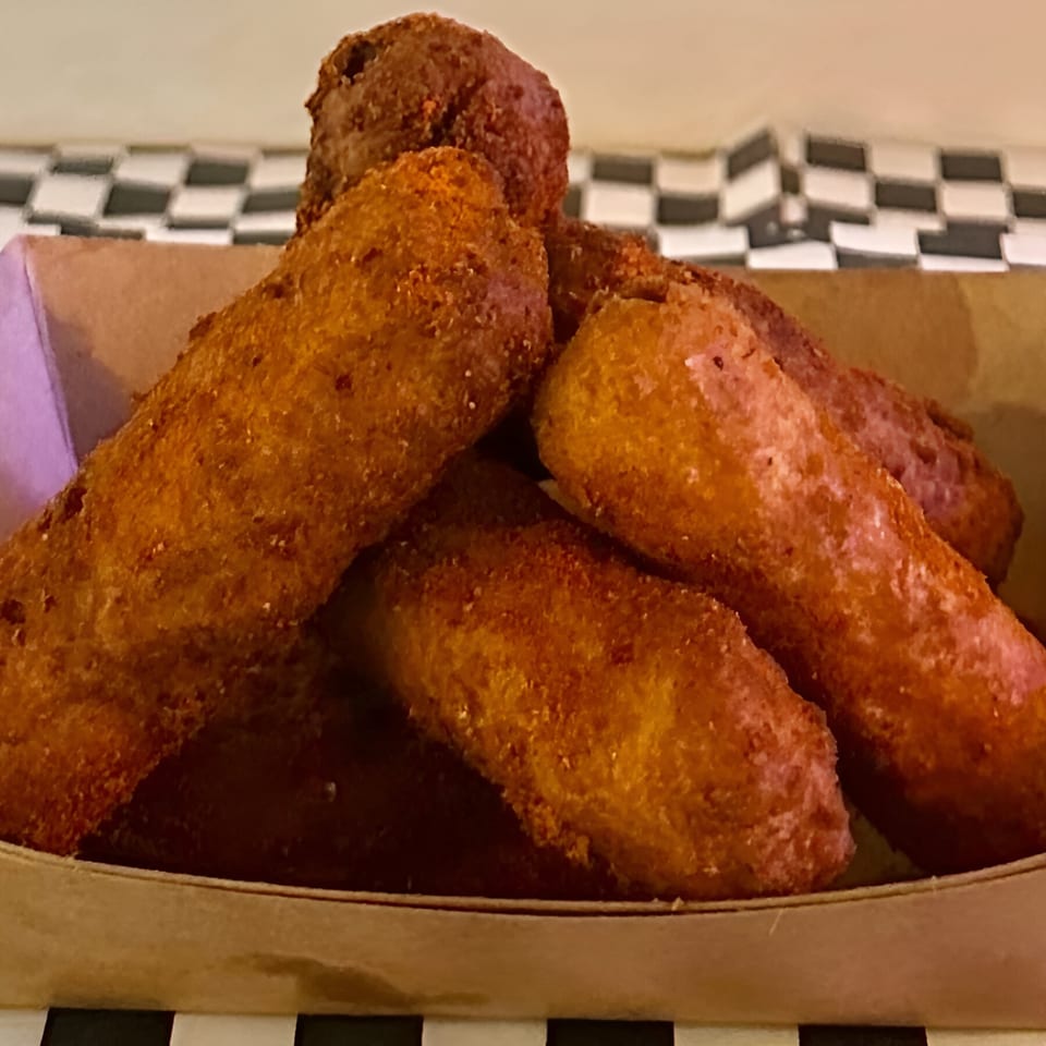 Golden brown Made Burgers corn dogs piled in a paper tray on a checkered surface.