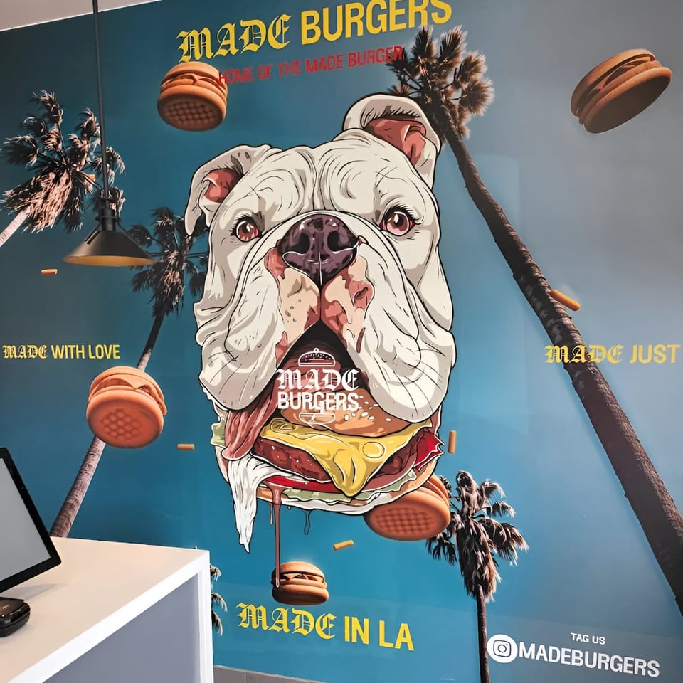 Made Burgers wall art featuring a bulldog's head with a burger for a mouth, palm trees, and flying burgers.