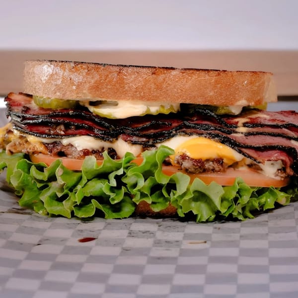 A Made Burgers sandwich with pastrami, cheese, burger patty, lettuce, tomato, and pickles.