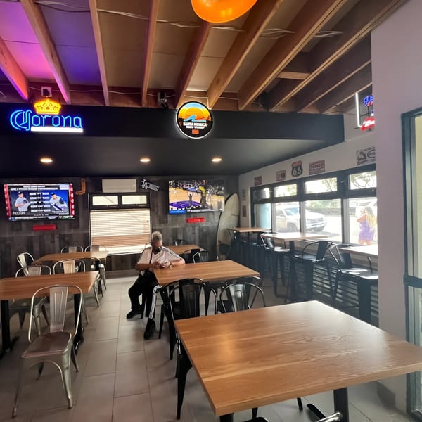 A Made Burgers restaurant interior with a person seated at a table, TVs, and neon signs.
