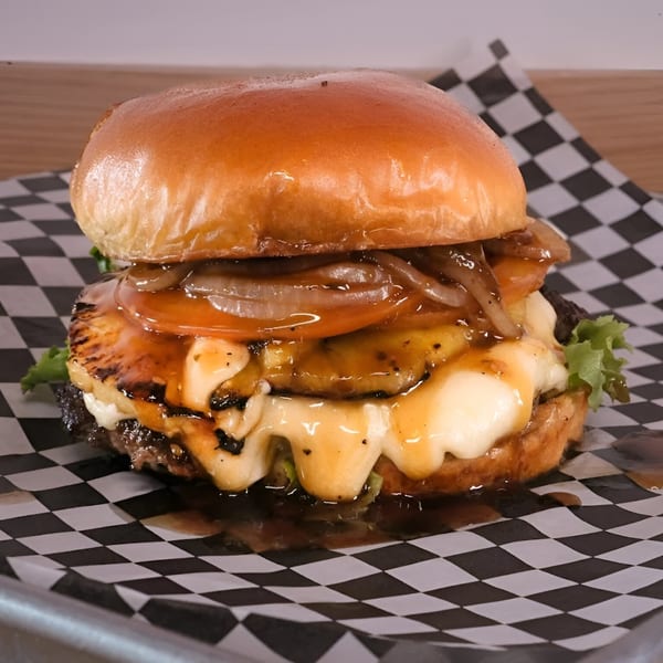 Made Burgers' burger with melted cheese, grilled pineapple, caramelized onions, and sauce on checkered paper.