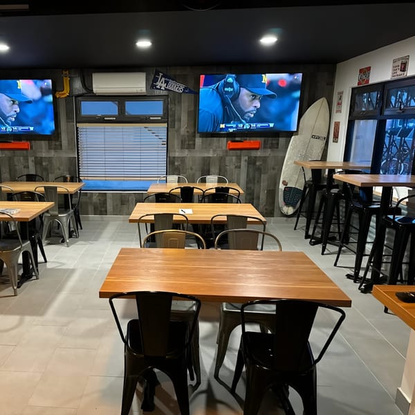 Interior of Made Burgers with wooden tables, metal chairs, two TVs, and a surfboard.