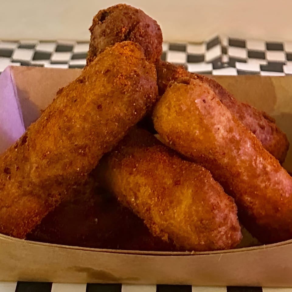 Golden-brown fried mozzarella sticks piled in a cardboard tray, with a checkered background.