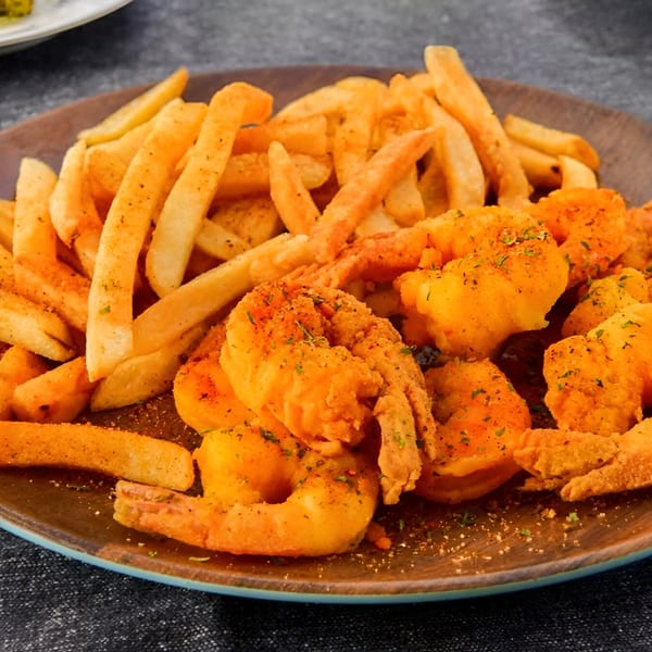 Crispy golden french fries and fried shrimp seasoned with herbs on a brown plate.