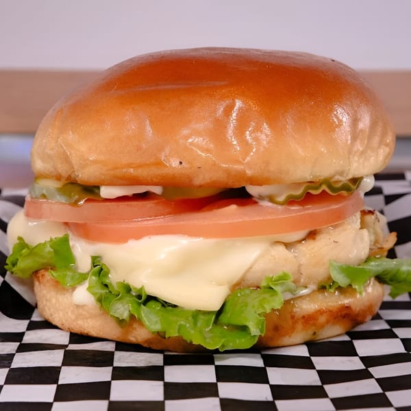 A Made Burgers chicken sandwich with lettuce, tomato, pickles, and melted cheese on a bun.