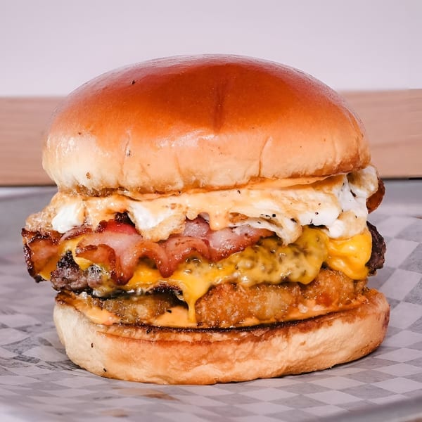 A Made Burgers burger with bacon, cheese, hash brown, and a fried egg on a checkered wrapper.