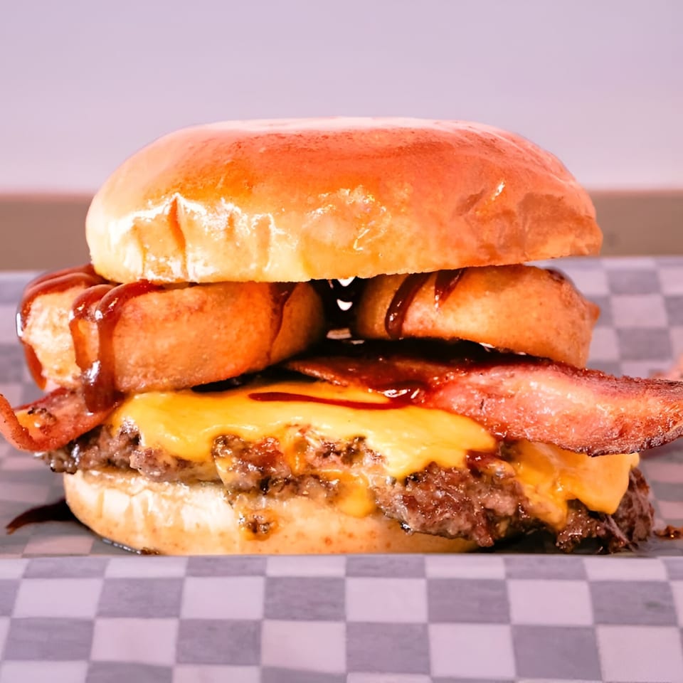Made Burgers' burger with bacon, melted cheese, onion rings, and barbecue sauce on a bun.