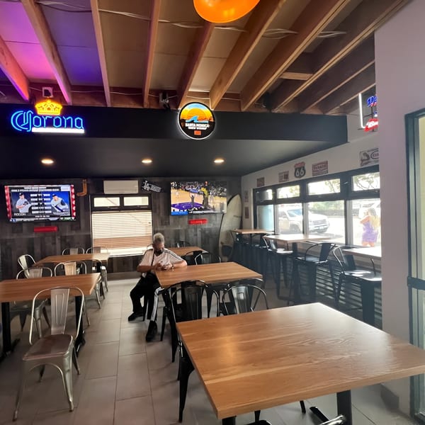 Interior of Made Burgers with a customer, wooden tables, metal chairs, and neon signs.